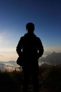 Rear view of silhouette boy standing on mountain against sky