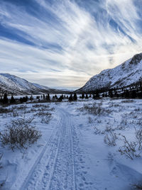 Snow covered road by mountains against sky