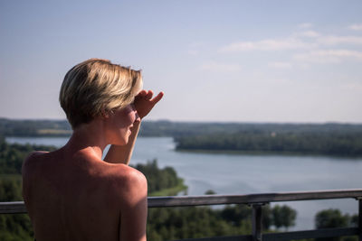 Rear view of young woman shielding eyes by railing against river