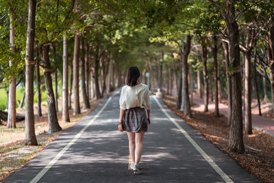 Rear view of woman walking on footpath amidst trees