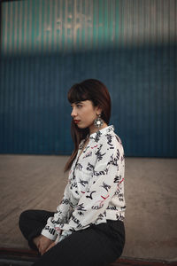 Young woman looking away while sitting against wall