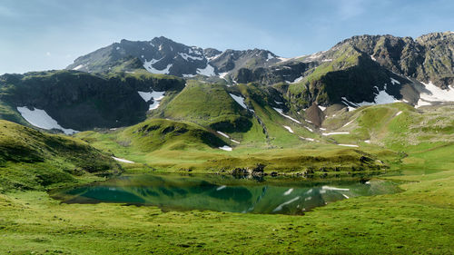 Mountain landscape with small glacial lake . mountain peaks with snow, green grass in the foreground