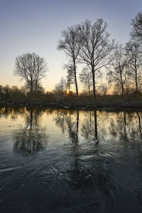 Silhouette bare trees by lake against sky during sunset