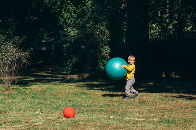 Side view of cute boy playing with large ball in park