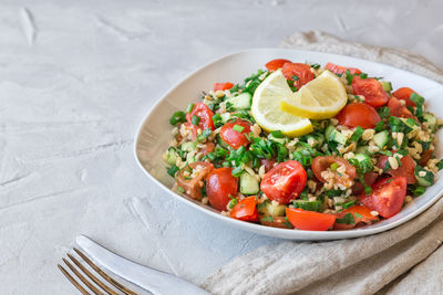 Tabbouleh salad on a dish on light gray concrete background. lebanese cuisine.