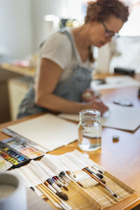 Artist painting in studio, paintbrushes in foreground