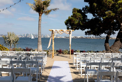 Square wooden wedding arch for outdoor beach yacht club wedding. white chairs and decorated arch 
