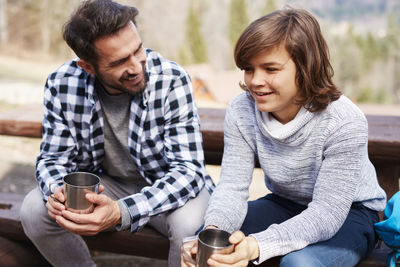 Smiling father and son having coffee while sitting on bench