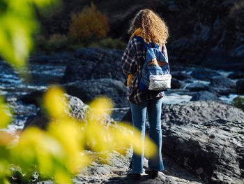 Young curly woman traveller looking at mountain river in autumn, traveller in beautiful nature