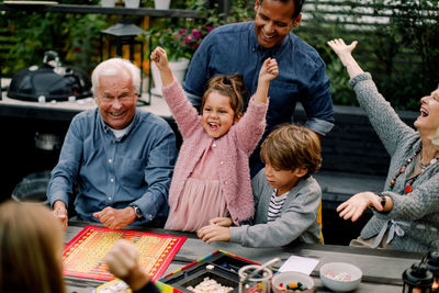 Cheerful multi-generation family playing board game on table while sitting in patio