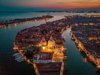 High angle view of illuminated buildings by sea against sky at sunset