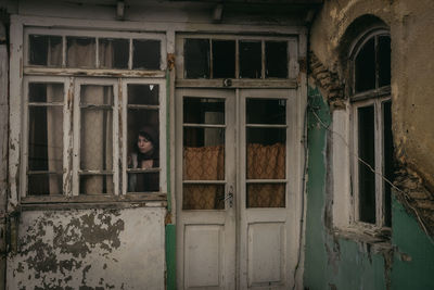Woman looking through window of old house