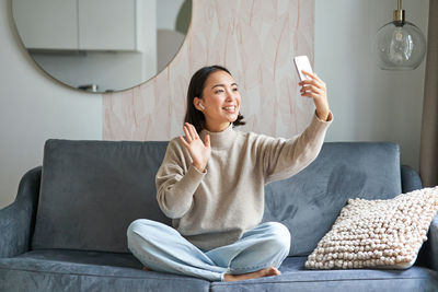 Young woman using mobile phone while sitting on sofa at home