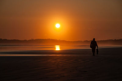 Rear view of silhouette man walking on beach at sunset