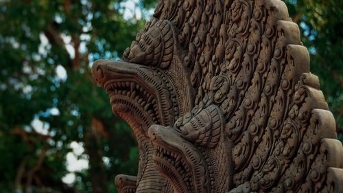 Close-up of naga statue against tree trunk