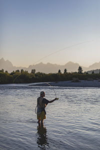 Side view of man fishing in lake against clear sky during sunset