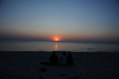Silhouette couple standing on beach against clear sky during sunset