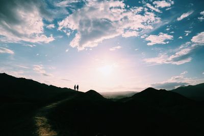 Silhouette friends standing on mountain at sunset