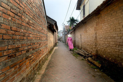Rear view of woman walking on road amidst brick wall