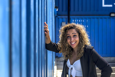 Portrait of smiling young woman standing against blue wall