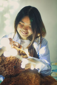 Smiling young woman with teddy bear in illuminated room