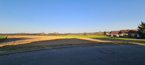 Road amidst field and houses against clear blue sky