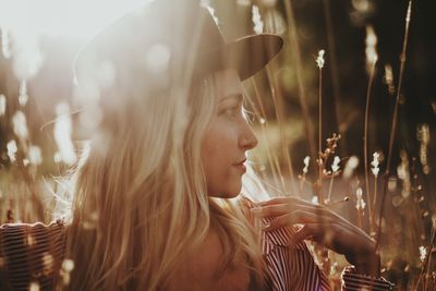 Close-up of young woman wearing hat on field during sunset