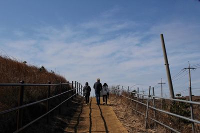 Rear view of family walking on footpath against sky