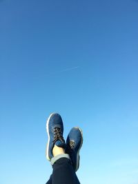 Low section of person with feet up against blue sky