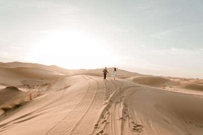 A couple in their wedding dresses walk barefoot through the desert at dawn. wedding concept