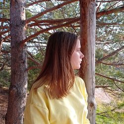 Close-up of young woman standing on tree trunk in forest