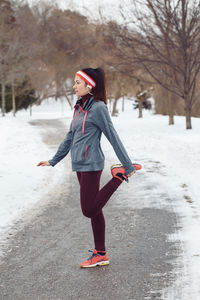 Full length of woman exercising on road during winter