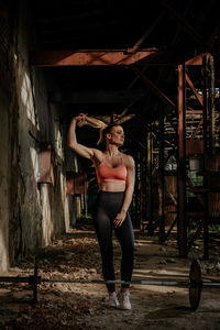 Full length of woman in sports clothing standing by barbell at abandoned building