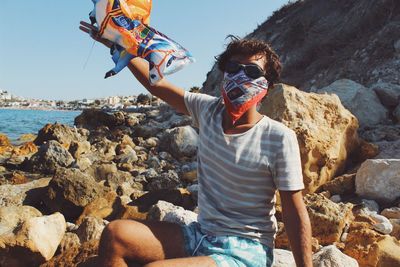 Portrait of man with scarf sitting on rocks at beach