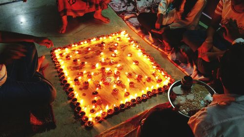 Low section of people sitting around lit diyas on floor