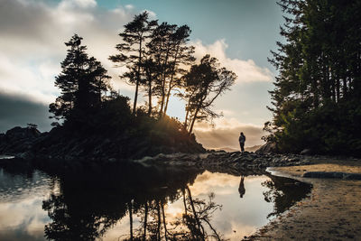 Man standing on rock by lake against sky