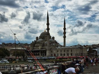 People walking in city against cloudy sky