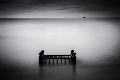 Silhouette people sitting on seat by sea against sky