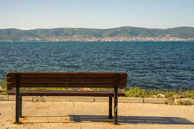 Empty bench by sea against clear sky