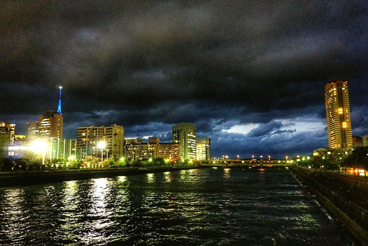 building exterior, architecture, illuminated, built structure, city, sky, water, night, cloud - sky, river, waterfront, cityscape, cloudy, tall - high, tower, skyscraper, weather, modern, storm cloud, dusk