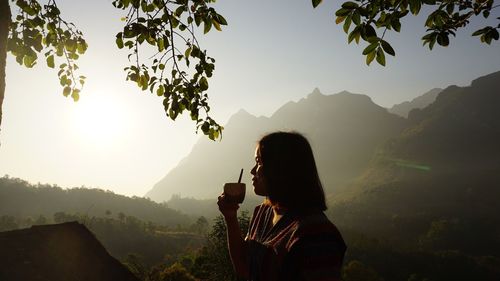 Woman holding coffee cup by mountains against sky