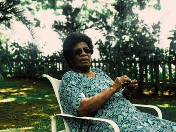 Portrait of woman wearing sunglasses sitting on chair in yard