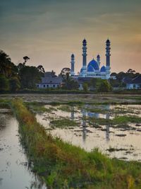 Scenic view of lake by buildings against sky during sunset