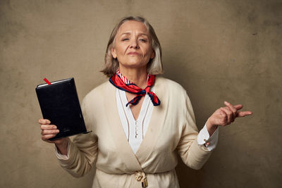 Portrait of woman holding smart phone while standing against wall