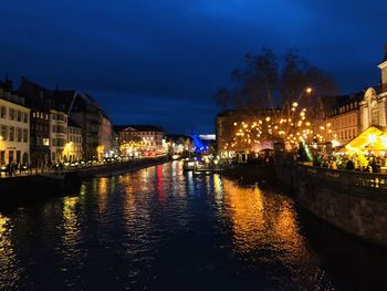 Illuminated buildings by river against sky at night