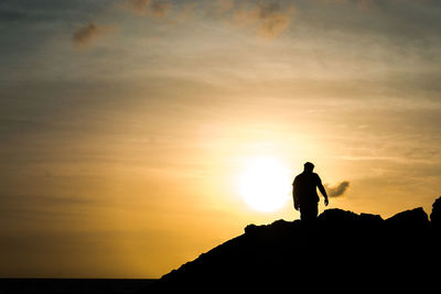 Silhouette man standing on rock against sky during sunset