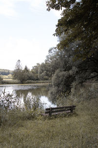 Bench by lake against sky