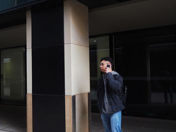 Young man talking on phone standing outside building