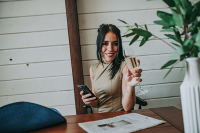 Woman using mobile phone while having wine at home