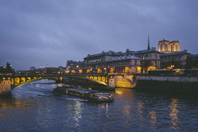 Illuminated bridge over river against sky in city